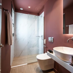 A modern bathroom with a glass shower enclosure, a white sink, and a toilet. - Metropole Urban Hotel (Heraklion)