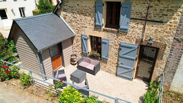 A small wooden house with a sloped roof, a balcony with outdoor furniture, and a stone wall. - Small village house in the heart of Normandy! (Ferrières-la-Verrerie)
