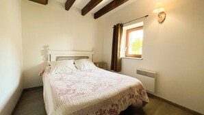 A bedroom with a bed, a window with curtains, a wall-mounted light, and a radiator. - Small village house in the heart of Normandy! (Ferrières-la-Verrerie)