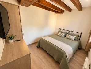 Ein Schlafzimmer mit einem Bett, einem Nachttisch mit Pflanze und einem an der Wand montierten Fernseher.