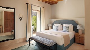 Ein Schlafzimmer mit Bett, Nachttischen, einer Bank, einem Spiegel und Blick durch ein Fenster.