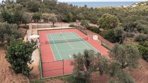 Ein Tennisplatz, umgeben von Bäumen, mit Blick auf das Meer.