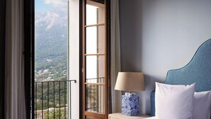 A hotel room with a bed, a nightstand with a lamp, and a view of a mountainous landscape through an open window. - Hotel Son Bunyola (Banyalbufar)