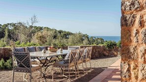 Un espace extérieur aménagé pour les repas, avec une table et des chaises, un mur en pierre et une vue sur la mer.
