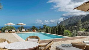 Un espace piscine doté de chaises longues et de parasols, offrant une vue sur un paysage montagneux.