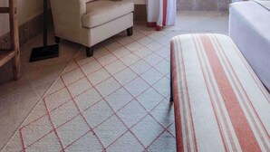 Ein Hotelzimmer mit einem Bett, einem Sessel, einem Tisch mit Lampe, einem Gemälde und einem fenster mit Vorhängen.
