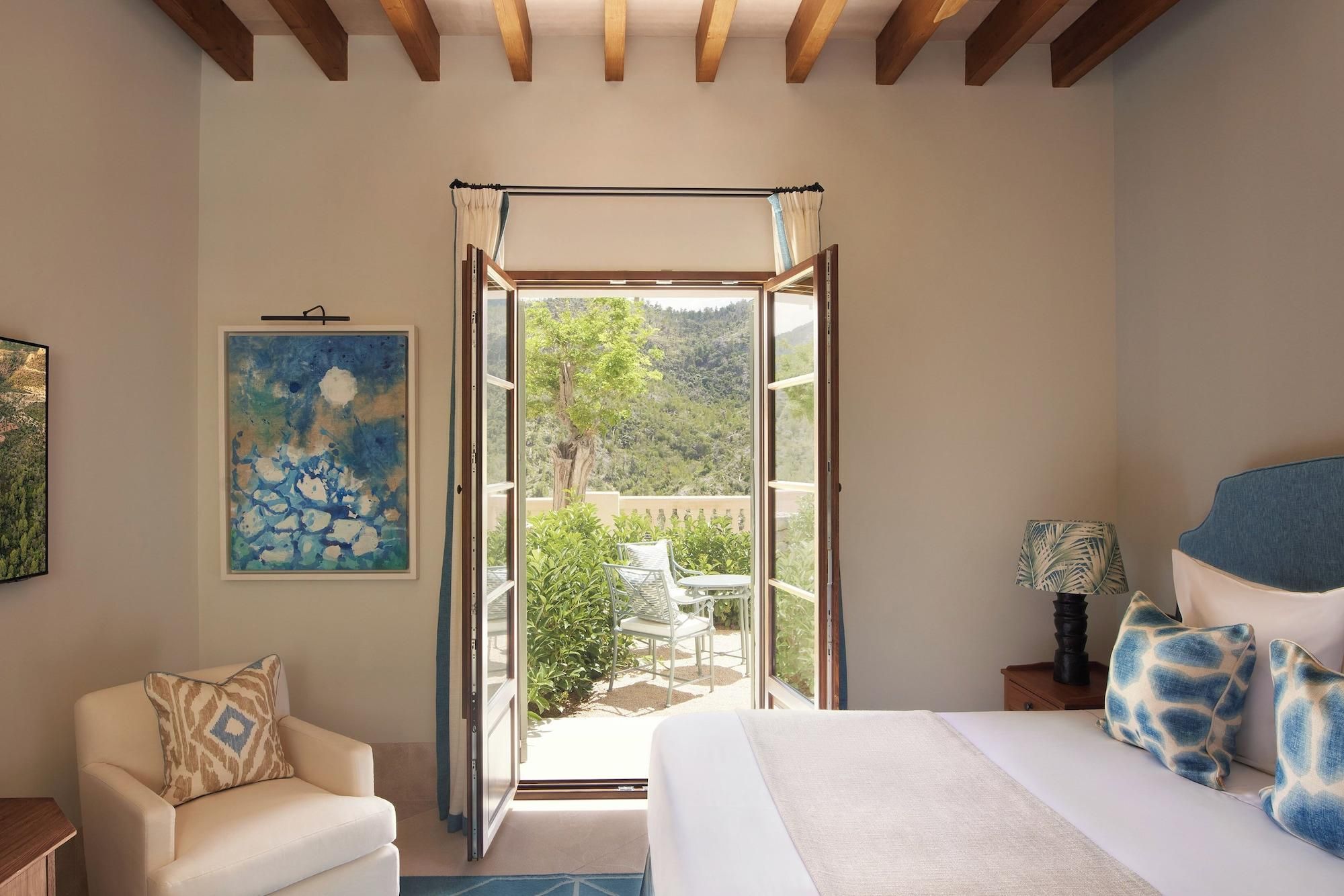 A bedroom with a bed, a chair, a nightstand, a painting, and a view of an outdoor patio.