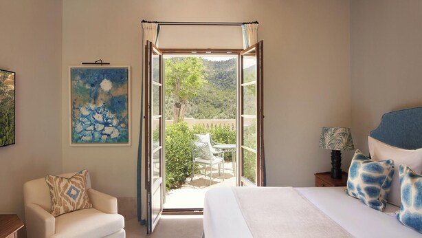 Une chambre à coucher comprenant un lit, une chaise, une table de chevet, un tableau et donnant sur une terrasse extérieure.