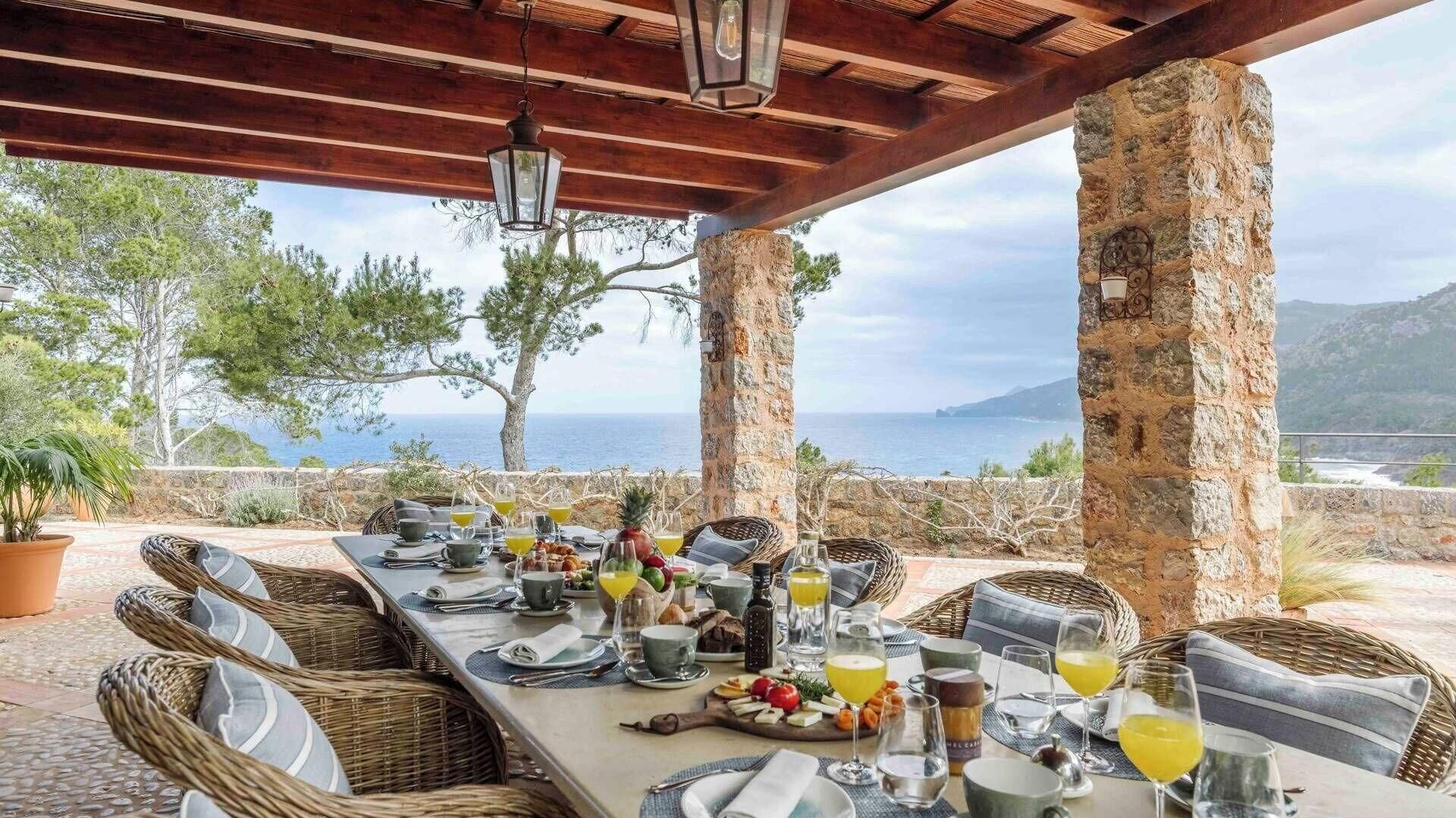 Un espace extérieur aménagé pour les repas, avec des piliers en pierre, des meubles en osier et une vue sur la mer.