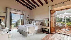 A bedroom with a large bed, a nightstand, a lamp, and a view of the outdoors. - Hotel Son Bunyola (Banyalbufar)