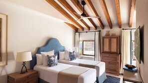 Un dormitorio con dos camas, una mesita de noche, un aparador, un ventilador de techo y una ventana con cortinas.