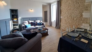 Un salon chaleureux avec un canapé, une table basse et une bibliothèque. Il y a un mur en pierre et une fenêtre avec des rideaux.