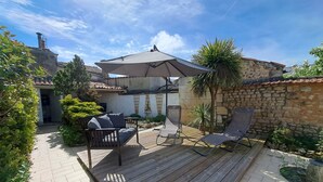 Une terrasse dotée d’une plateforme en bois, d’un canapé confortable, d’un fauteuil de relaxation et d’un grand parasol offrant de l’ombre.