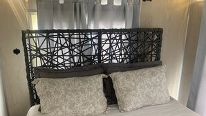 Una cama con colchón blanco, manta gris y almohadas estampadas.