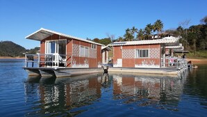 Una casa flotante con terraza y zona cubierta, ubicada en aguas tranquilas bajo un cielo despejado.