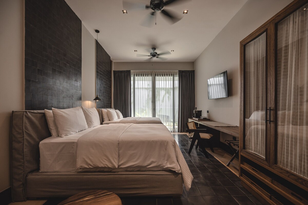 Una habitación de hotel moderna con dos camas, un escritorio, un televisor y un ventanal con cortinas.