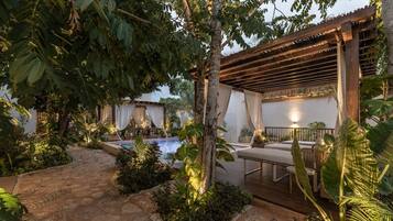 A pool area with a pergola, seating, and lush greenery.