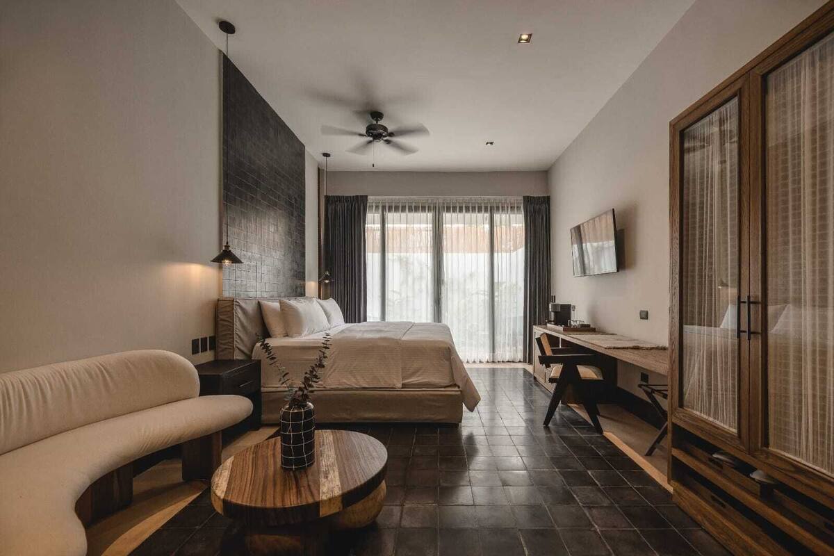 Una habitación de hotel moderna con cama, sofá, escritorio y un ventanal con cortinas.