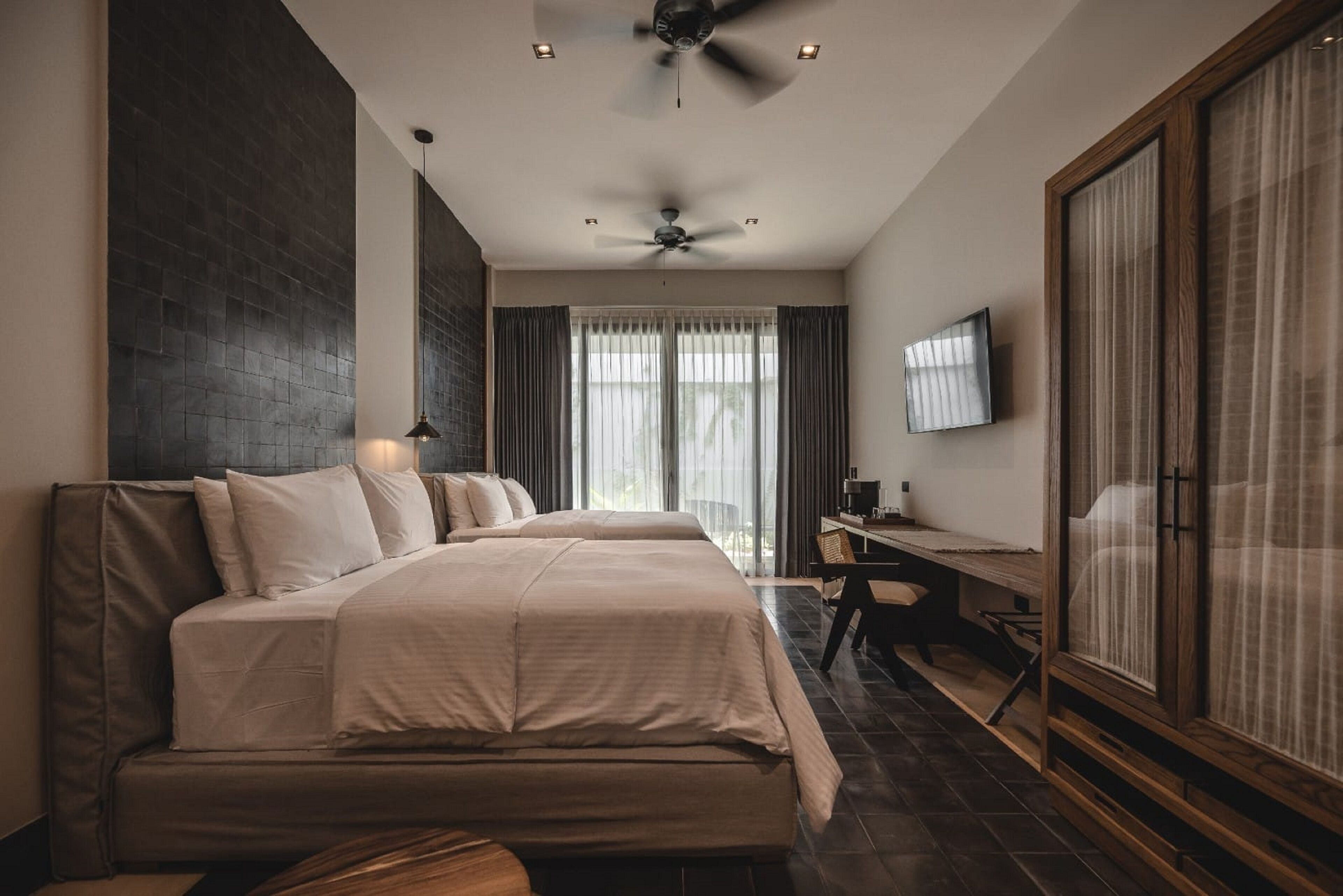 Una habitación de hotel moderna con una cama grande, un escritorio, un televisor y un ventilador de techo.