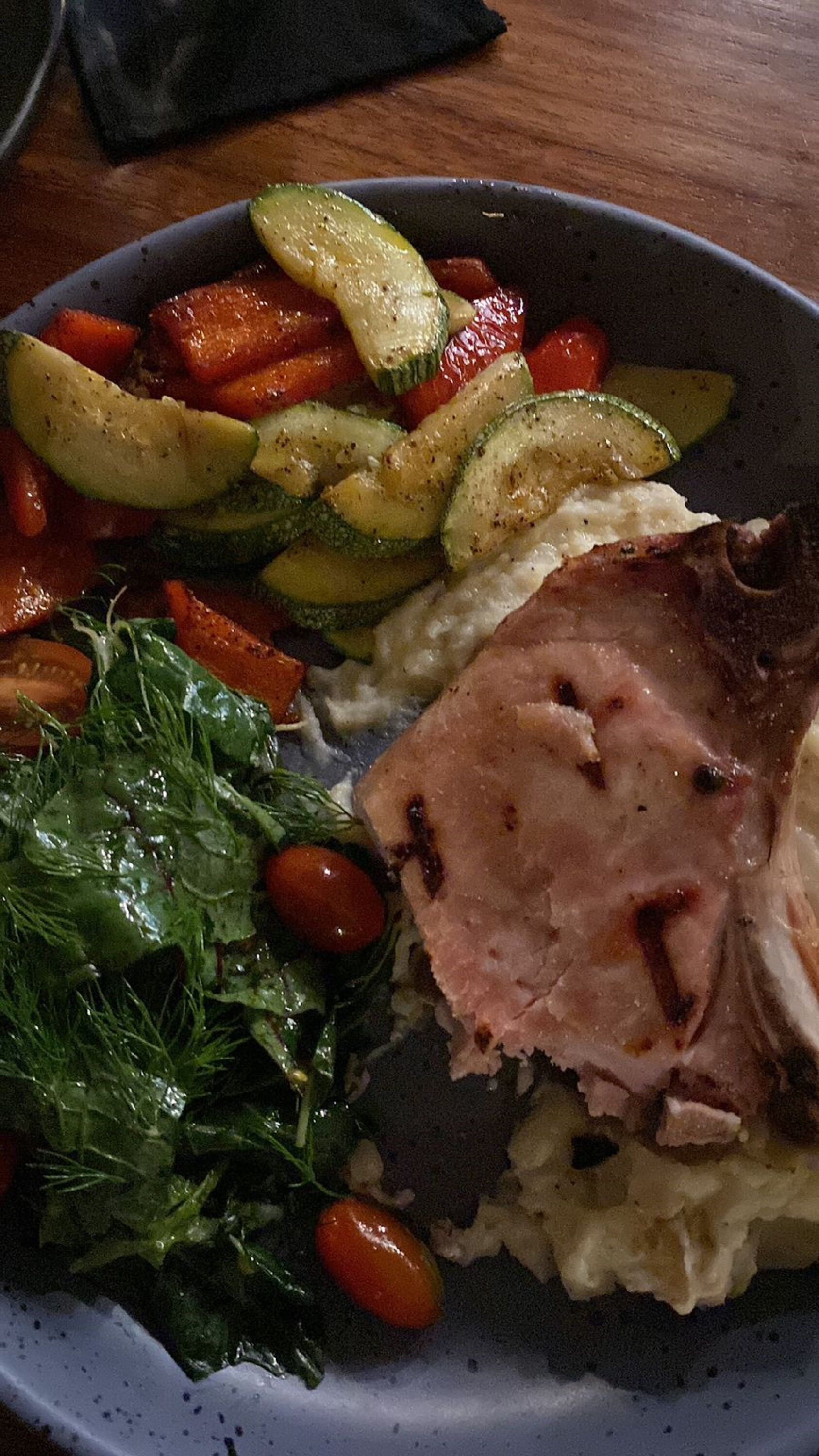 A plate with roasted vegetables, a slice of ham, and greens.