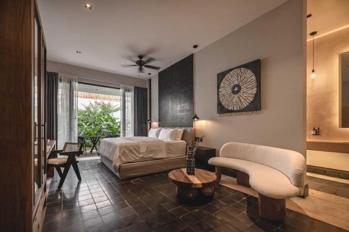 Una habitación de hotel moderna con una cama, un sofá, una mesa redonda y una zona de comedor con una mesa y sillas.