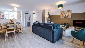 A modern living room with a sofa, dining table, and chairs. There is a TV on a stand and a painting on the wall. - Spacious House, Incredible Location, FREE Parking! (Chester)