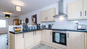 A modern kitchen with light wood cabinets, a black countertop, a built-in oven, and a stainless steel range hood. - Spacious House, Incredible Location, FREE Parking! (Chester)