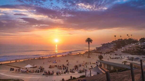 A beach scene with a sunset, palm trees, and a road.