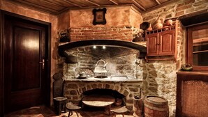 Eine rustikale Küche mit Kamin aus Stein, Holzschränken und Fliesenboden.