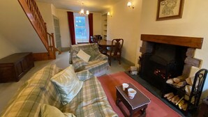 A cozy living room with a fireplace, plaid sofas, a wooden coffee table, and a staircase. - Remarkable 3-bed House in Millom (Millom)