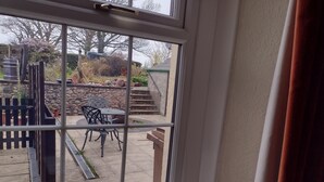 A view through a window of a patio area with a stone wall, a wooden fence, and outdoor furniture. - Remarkable 3-bed House in Millom (Millom)