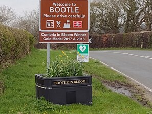A welcome sign for Bootle, a Cumbria in Bloom winner, and a public access defibrillator sign. - Remarkable 3-bed House in Millom (Millom)