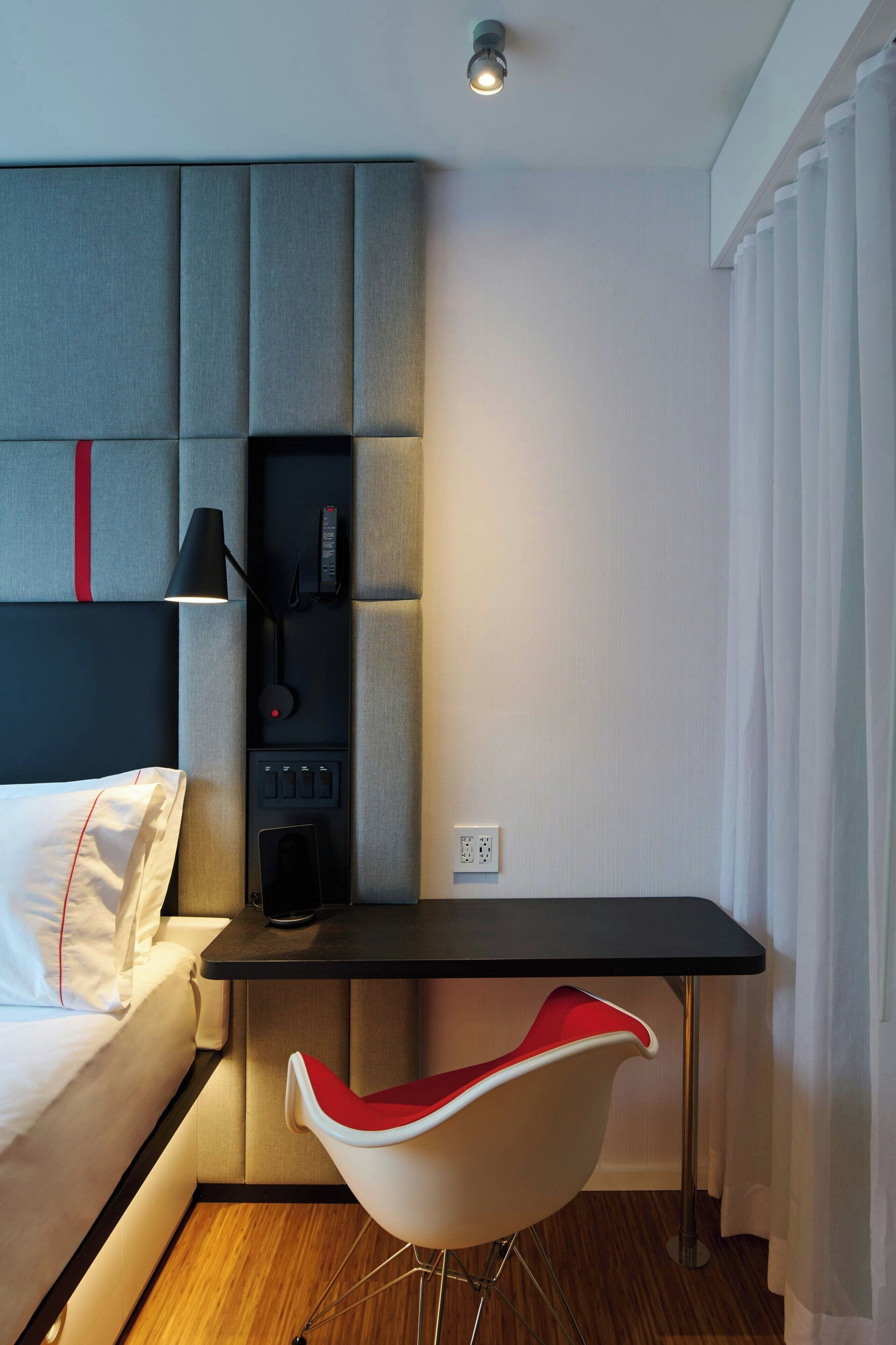 Una habitación de hotel moderna con una cama, un escritorio, una silla y un panel de control.