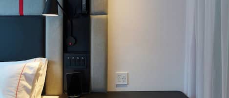 Une chambre d’hôtel moderne équipée d’un lit, d’un bureau, d’une chaise et d’un panneau de commande.