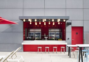 An outdoor bar area with a red counter, stools, and a red door.