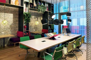 A modern meeting room with a long table, green chairs, and black pendant lights.