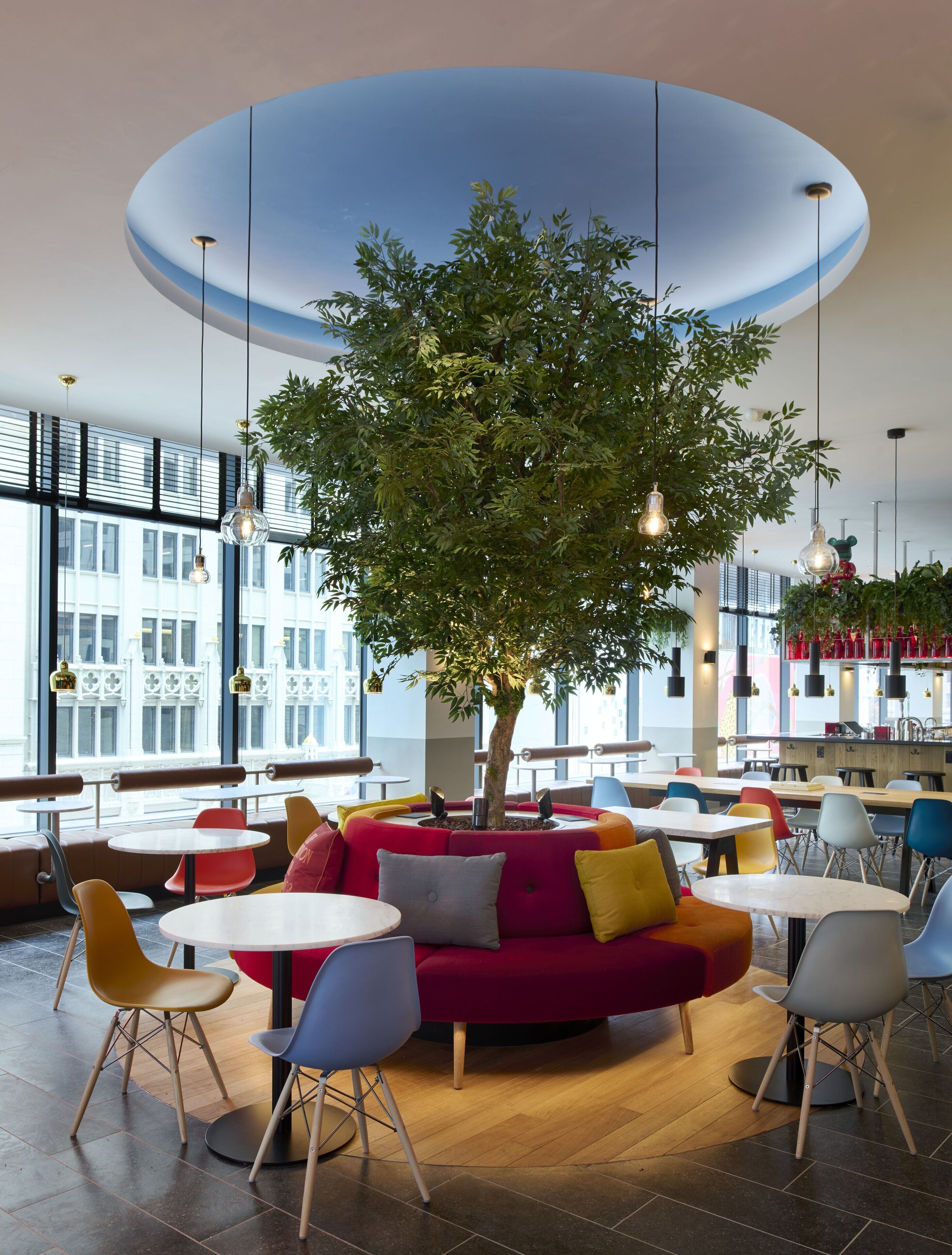 Un espace intérieur moderne, doté d’un arbre central, de tables rondes et de sièges aux couleurs vives.