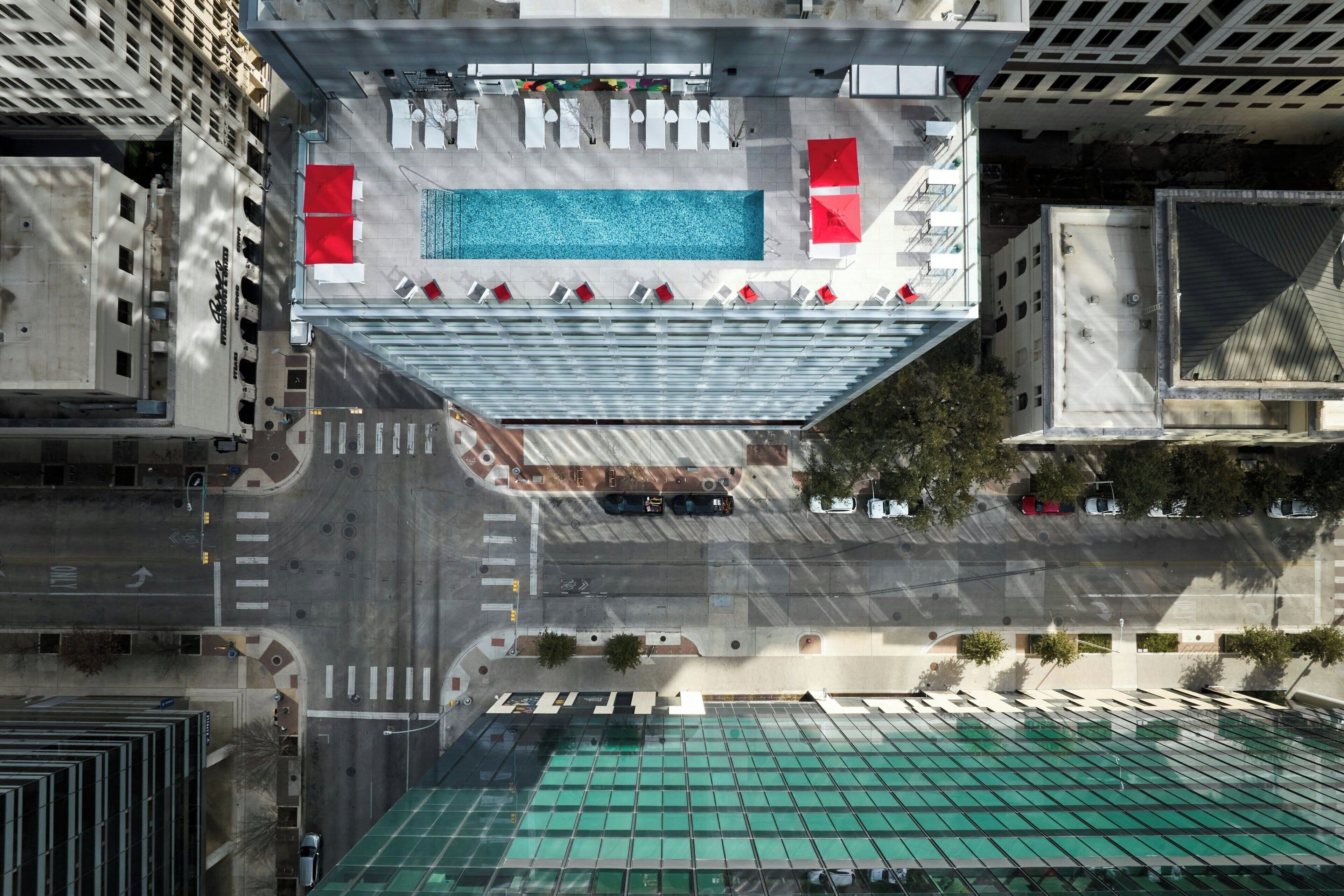 An aerial view of a hotel rooftop with a swimming pool, lounge chairs, and a green roof.