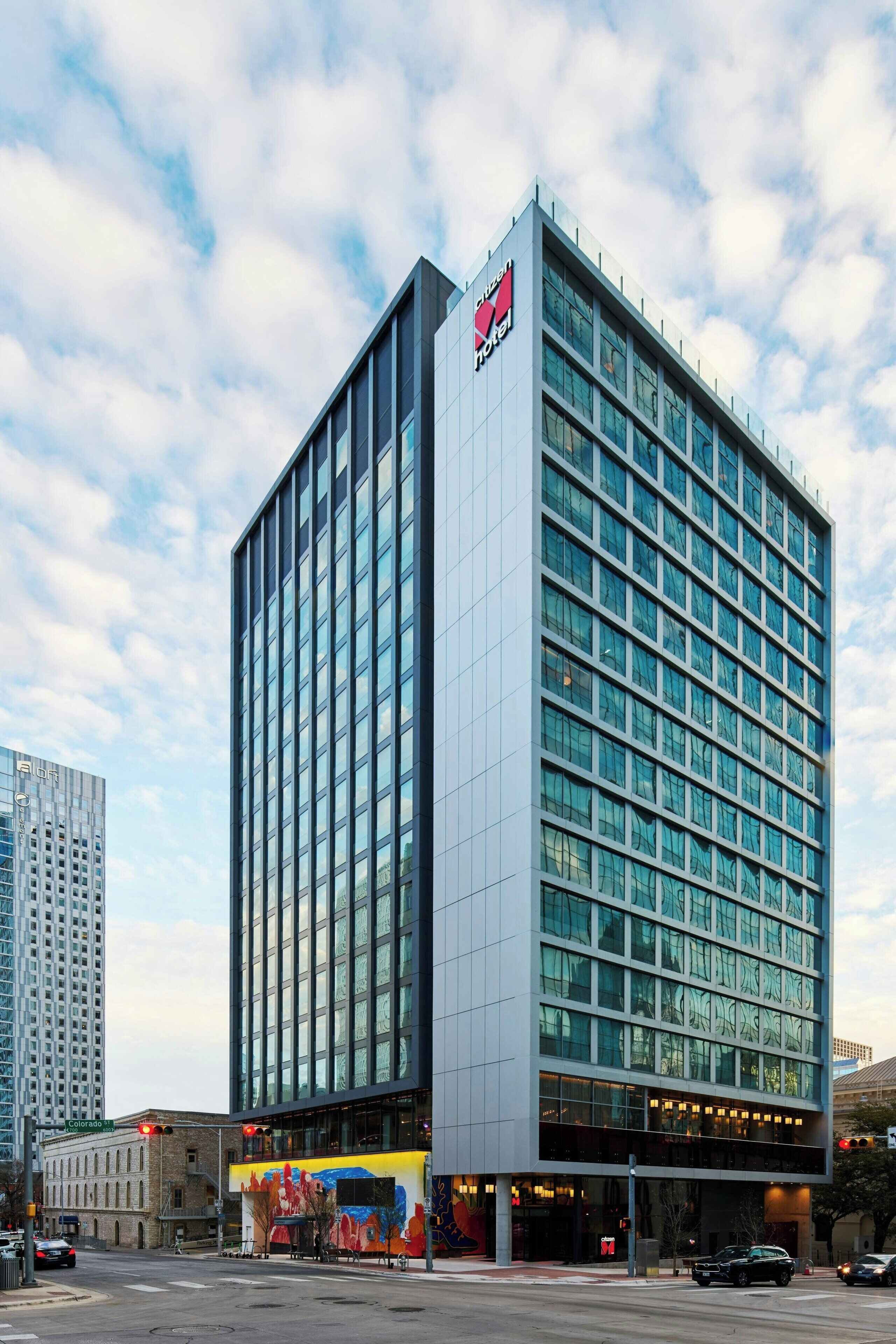 A modern hotel with a glass facade, multiple floors, and a prominent logo on the top.