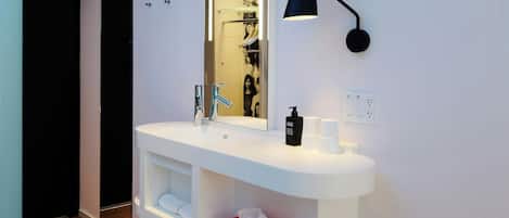 Ein modernes Badezimmer mit einem weißen Waschtisch, einem Spiegel, einer schwarzen Lampe und einem roten Hocker.