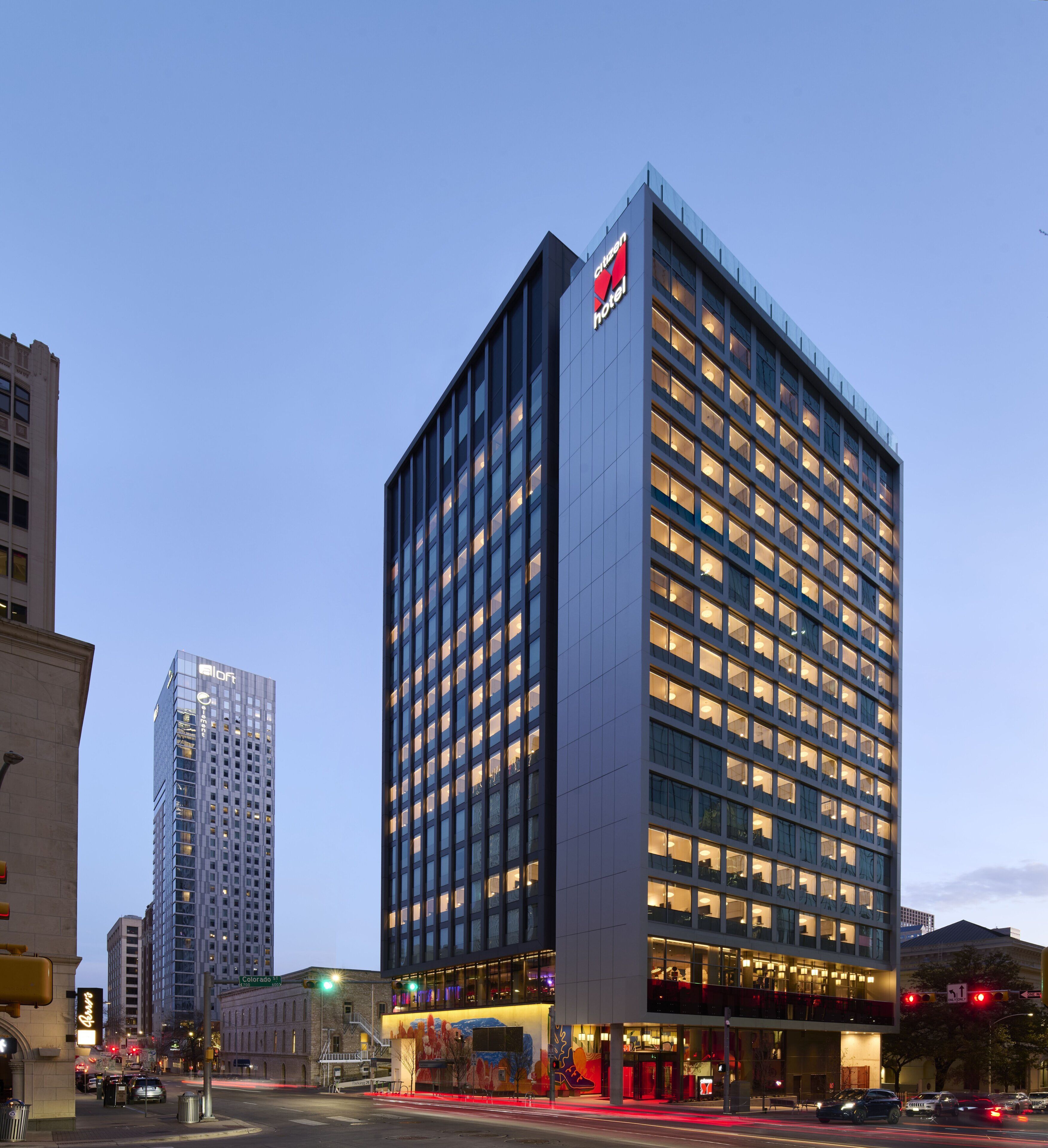 A modern hotel with a prominent logo on the facade, multiple floors, and a well-lit entrance area.