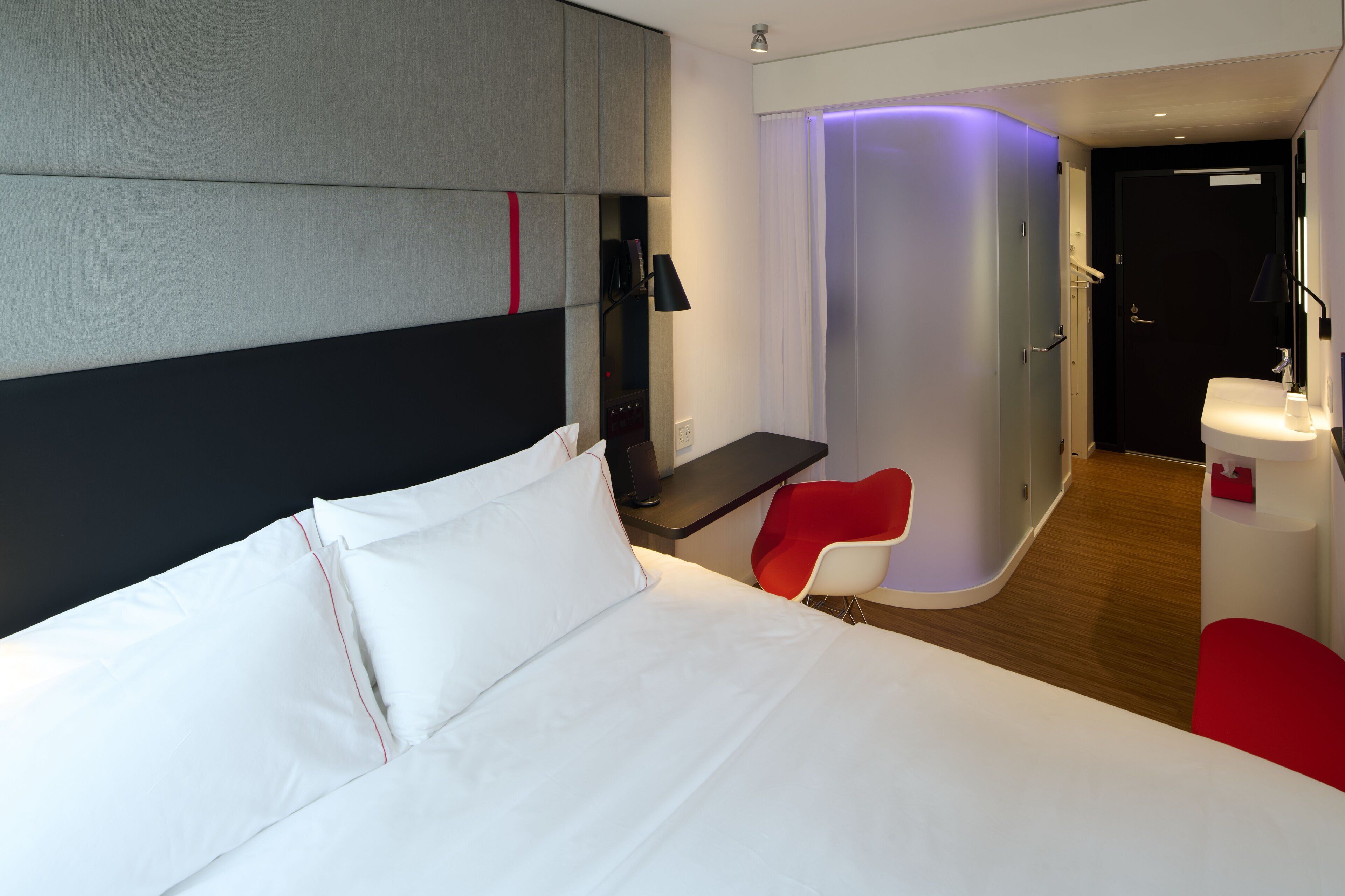 Habitació d'hotel moderna amb un llit gran, un escriptori, una cadira vermella i un bany separat.