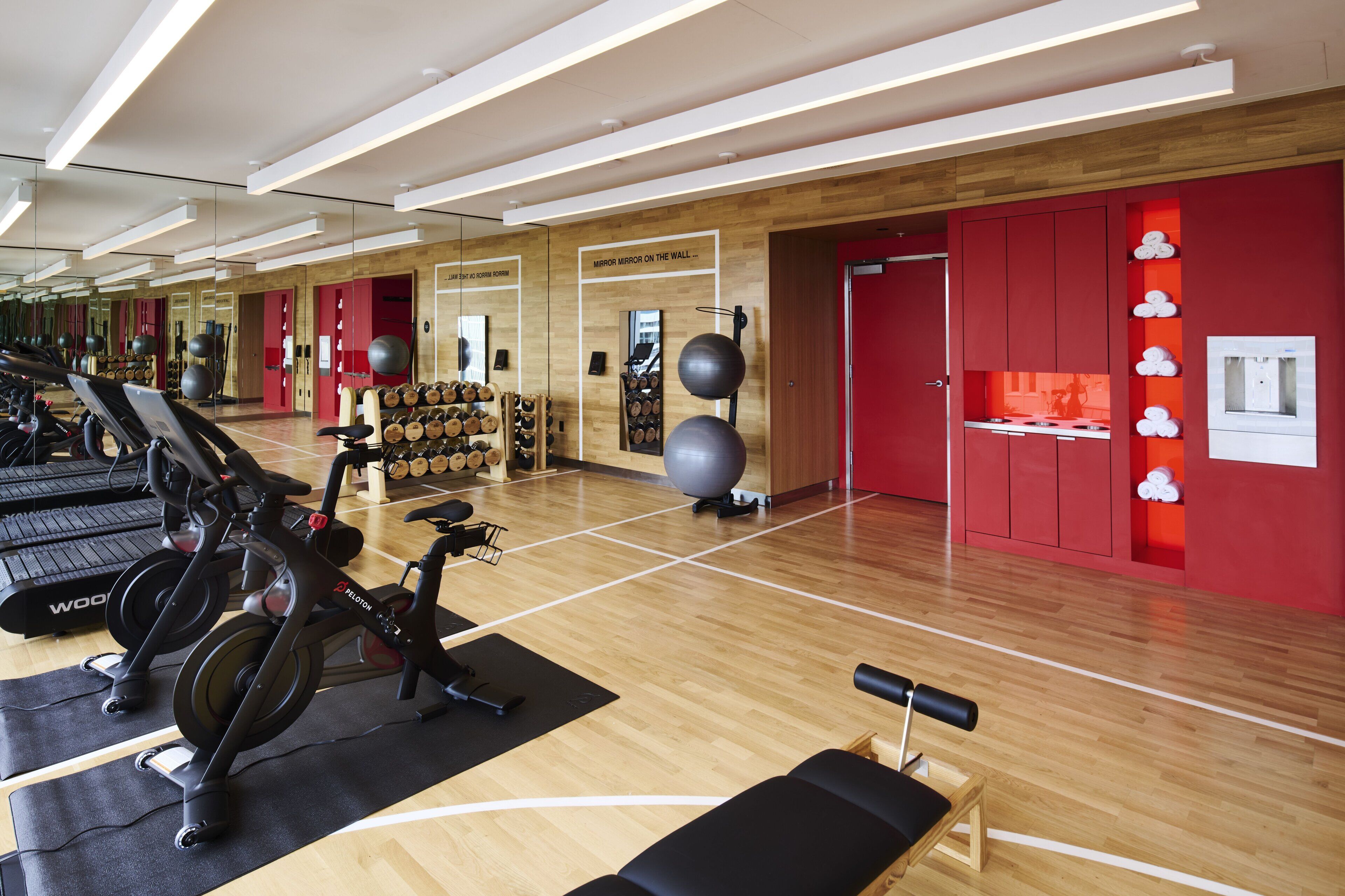 A gym with exercise equipment, wooden flooring, and red walls.