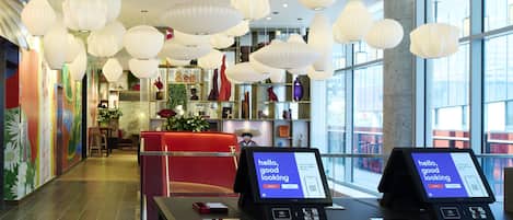 Un vestíbulo moderno con mostrador de recepción, quioscos digitales y lámparas decorativas colgantes.
