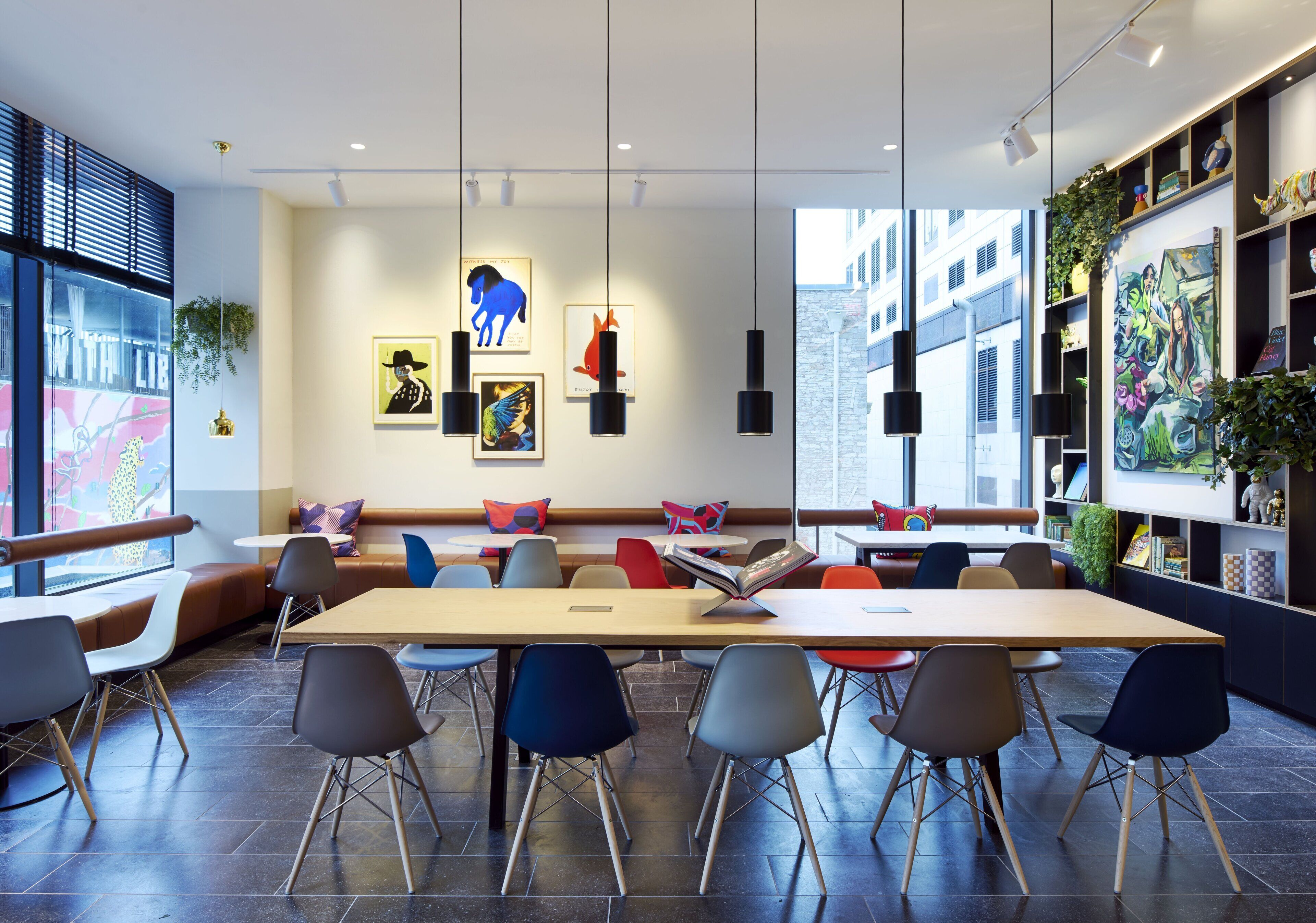 A modern, well-lit meeting room with a long table, multiple chairs, and a sofa with colorful cushions.