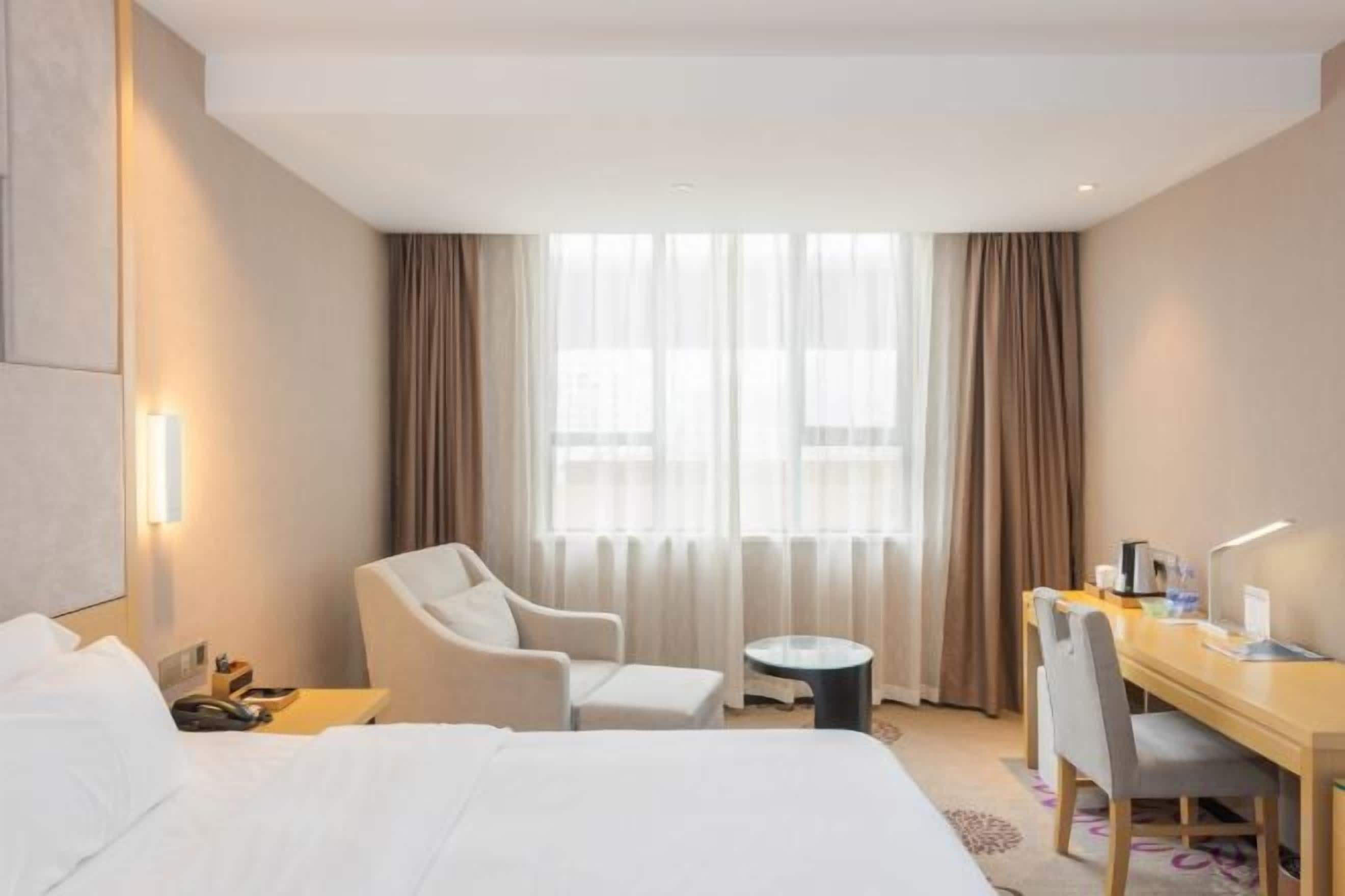 Une chambre d’hôtel avec un lit, un bureau, une chaise, une petite table ronde et une fenêtre avec des rideaux.