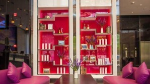 Un hall moderno con dos sofás morados, una mesa de centro negra y estanterías rojas con diversos objetos decorativos.
