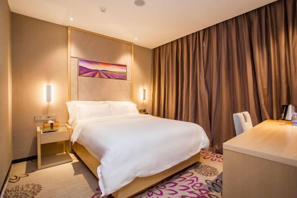 A hotel room with a bed, bedside tables, a desk, and a painting on the wall.