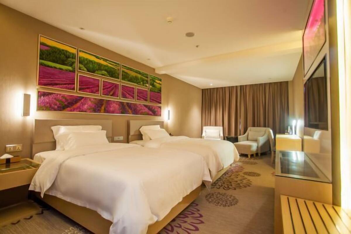 A hotel room with two beds, a large wall mural, a seating area with a sofa and armchairs, and a glass table.