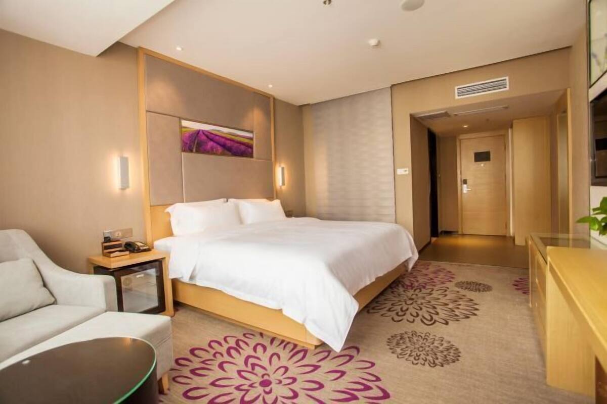 A modern hotel room with a large bed, a bedside table, a chair, and a desk.